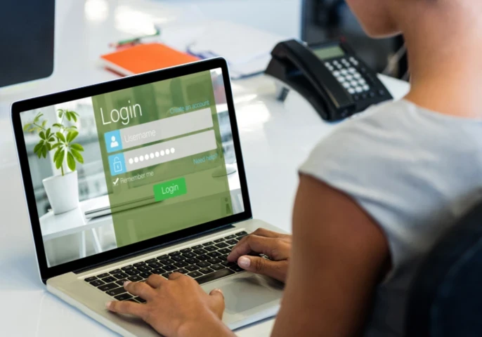 A woman sitting in front of a laptop with a login screen displayed.