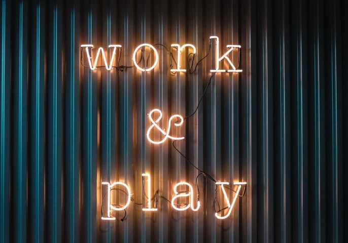 Neon lights spelling out "work & play" on a corrugated iron backdrop.