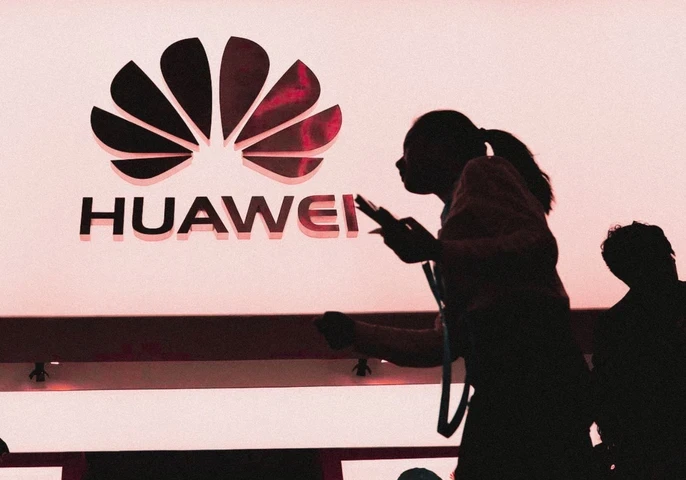 Silhouette of a woman walking past an illuminated Huawei logo.