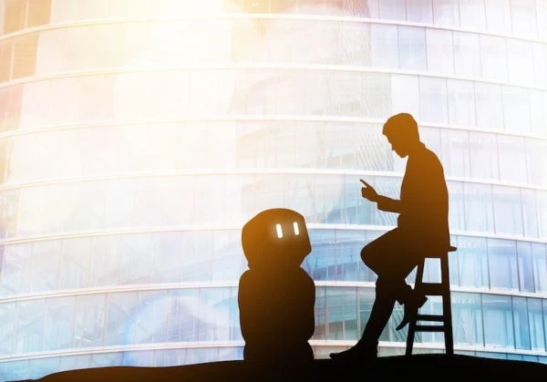 A photo of a person giving a robot instructions while the robot looks up at the person