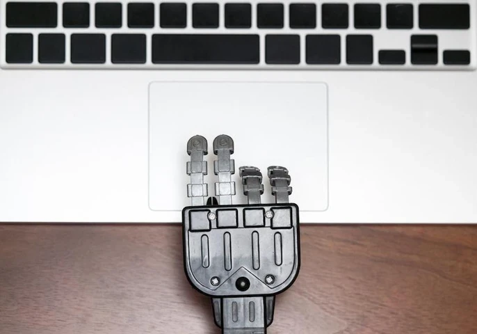 Robot hand using a trackpad on a laptop.