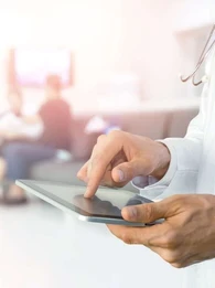 A doctor holding a tablet while patients wait in the background