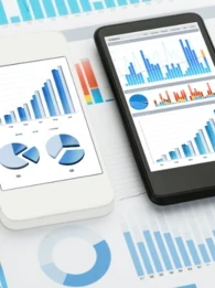Three smartphone laid on top of a pile of paper graphs.