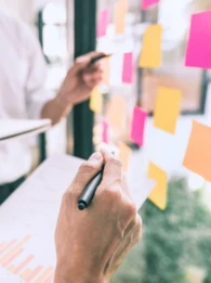 Two businesspeople standing in front of plexiglass with sticky notes discussing graphs.