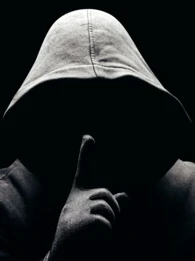 A person in a black hoodie holding up his finger to his mouth.