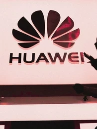 Silhouette of a woman walking past an illuminated Huawei logo.