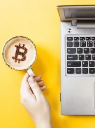 Coffee mug with Bitcoin latte art next to an Macbook laptop
