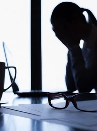 Woman sitting at a desk with her head in her hands.
