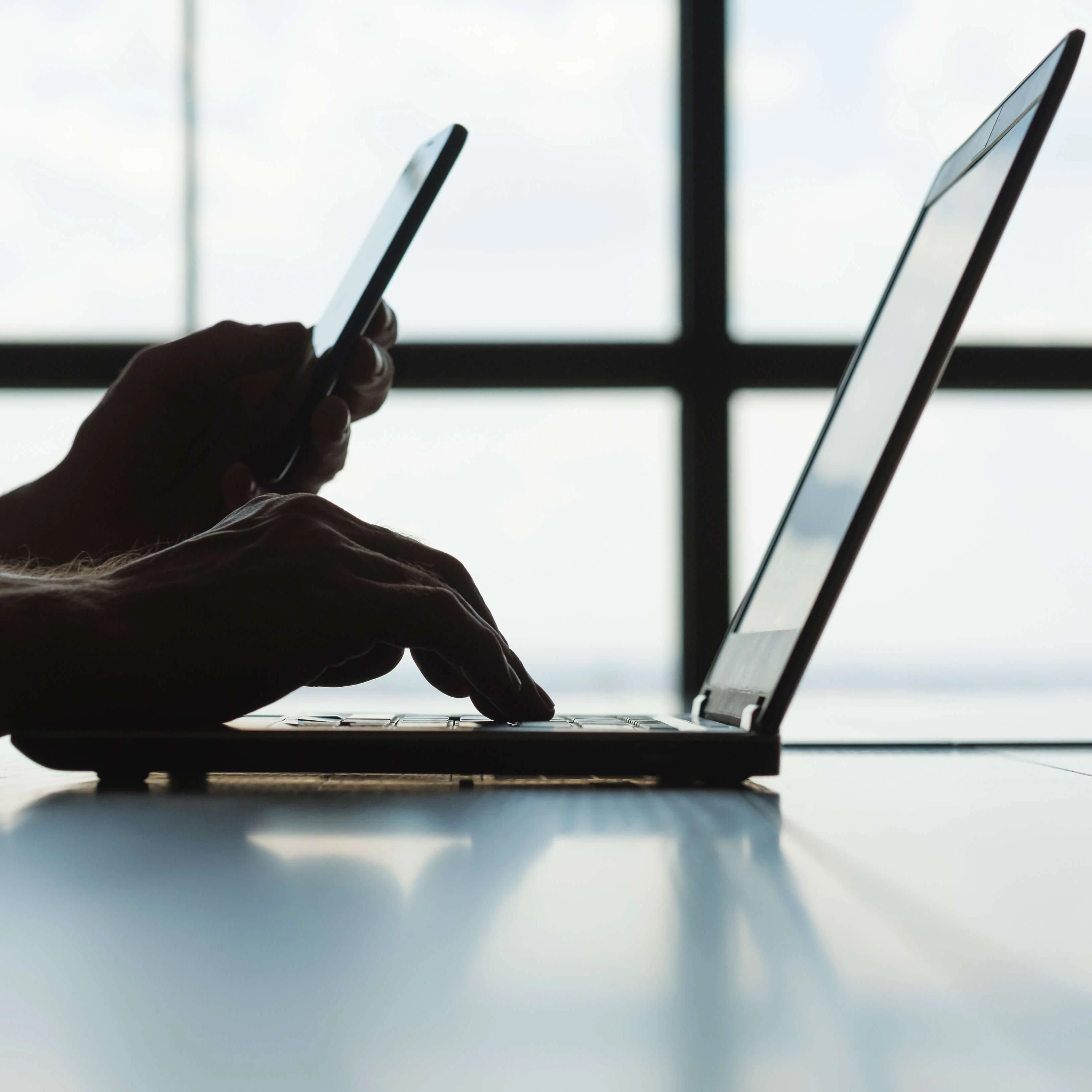 A person working on a laptop while holding a smartphone