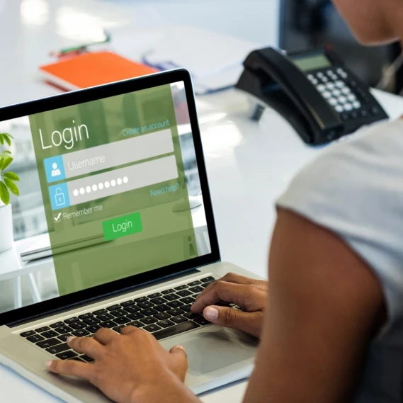 A woman sitting in front of a laptop with a login screen displayed.
