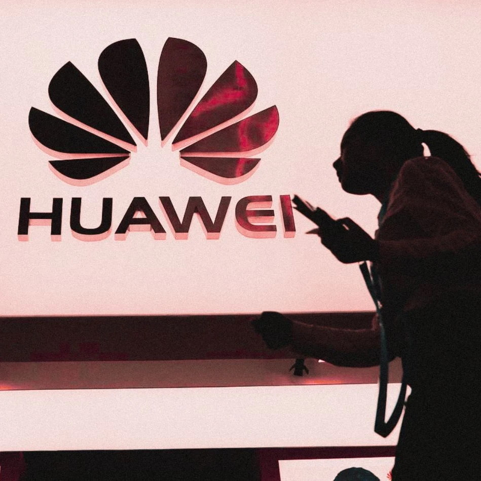 Silhouette of a woman walking past an illuminated Huawei logo.