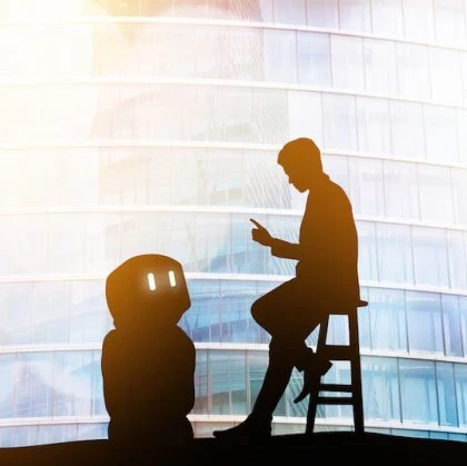 A photo of a person giving a robot instructions while the robot looks up at the person
