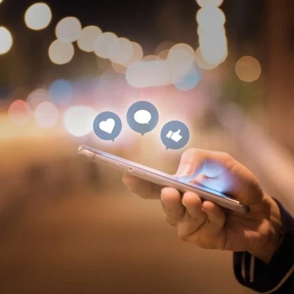 Person using a smartphone with Facebook reaction emojis floating above the screen