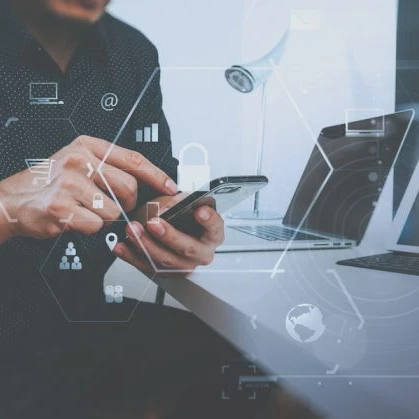 person on a smartphone next to two laptops