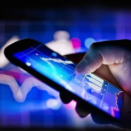 Hand holding a lit up smartphone with graphs on the screen in purple and blue.